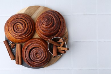 Photo of Delicious cinnamon roll buns and spices on white tiled table, top view