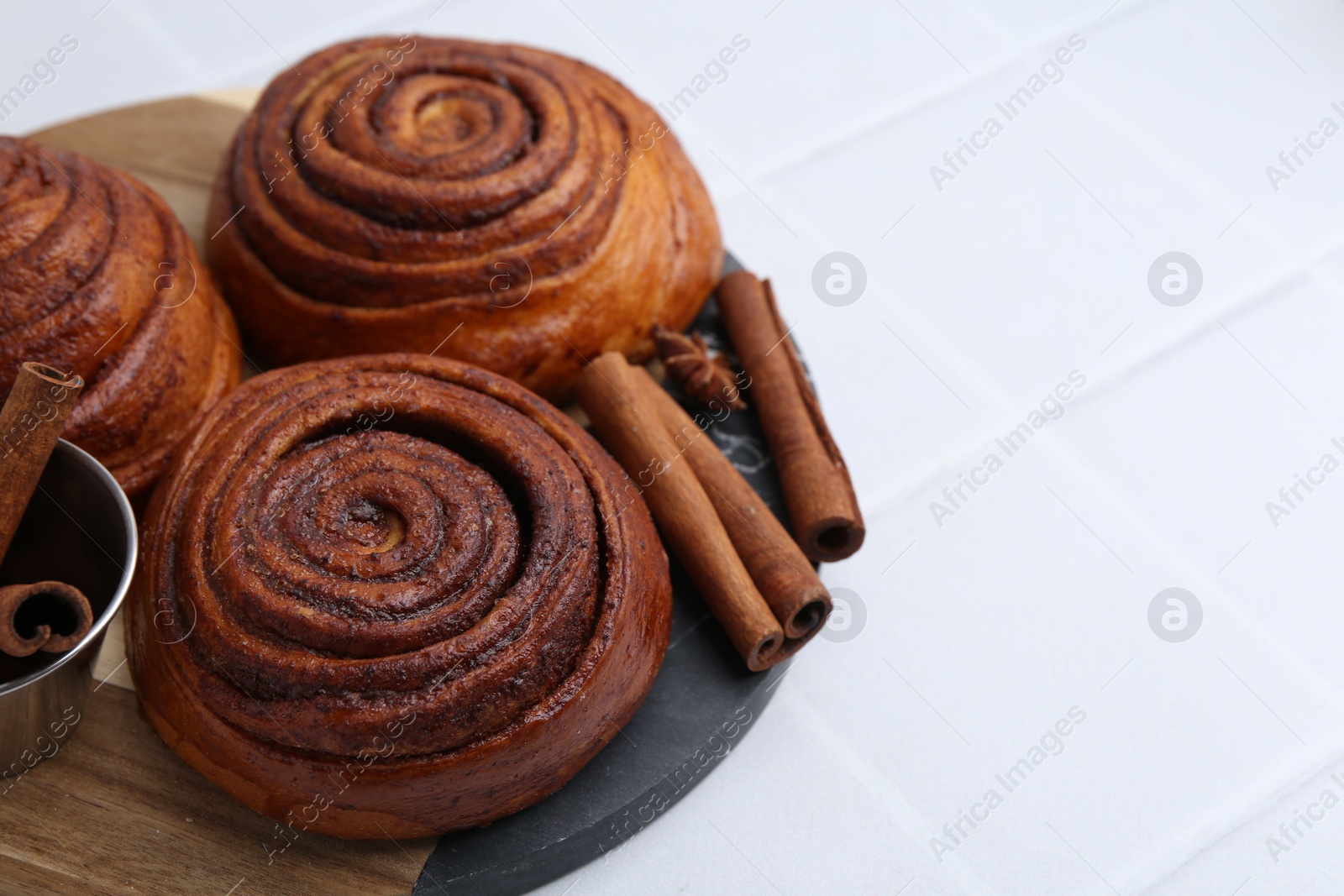 Photo of Delicious cinnamon roll buns and spices on white tiled table, closeup