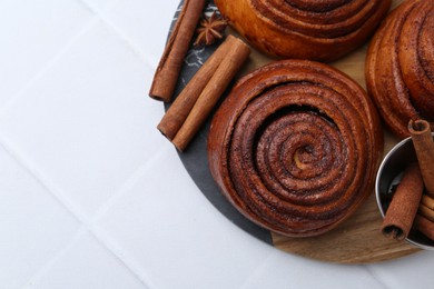 Photo of Delicious cinnamon roll buns and spices on white tiled table, top view