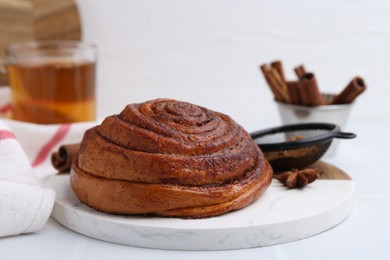 Photo of Delicious cinnamon roll bun and spices on white table, closeup