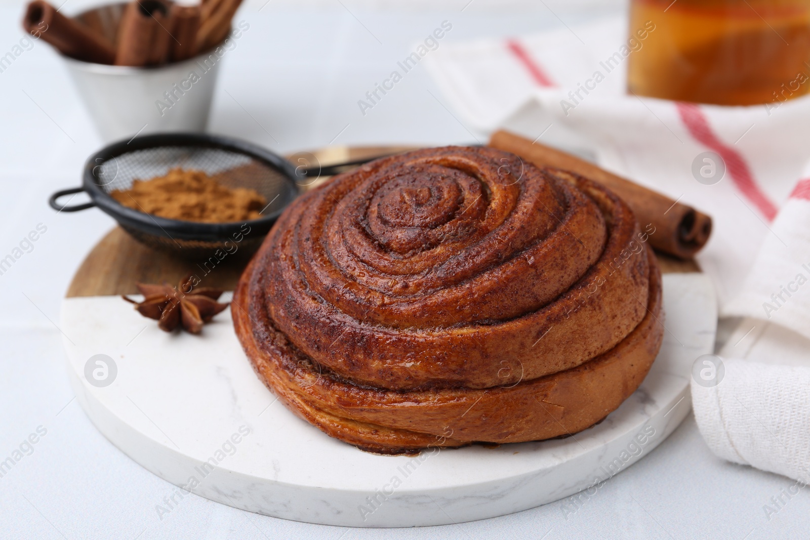 Photo of Delicious cinnamon roll bun and spices on white table, closeup