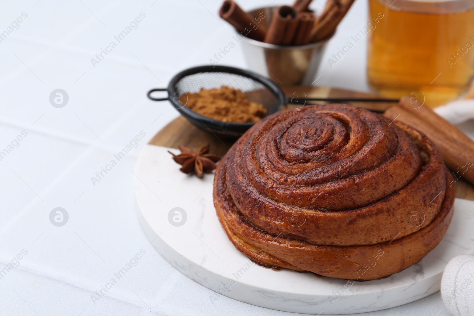 Photo of Delicious cinnamon roll bun, tea and spices on white tiled table, closeup