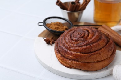 Photo of Delicious cinnamon roll bun, tea and spices on white tiled table, closeup