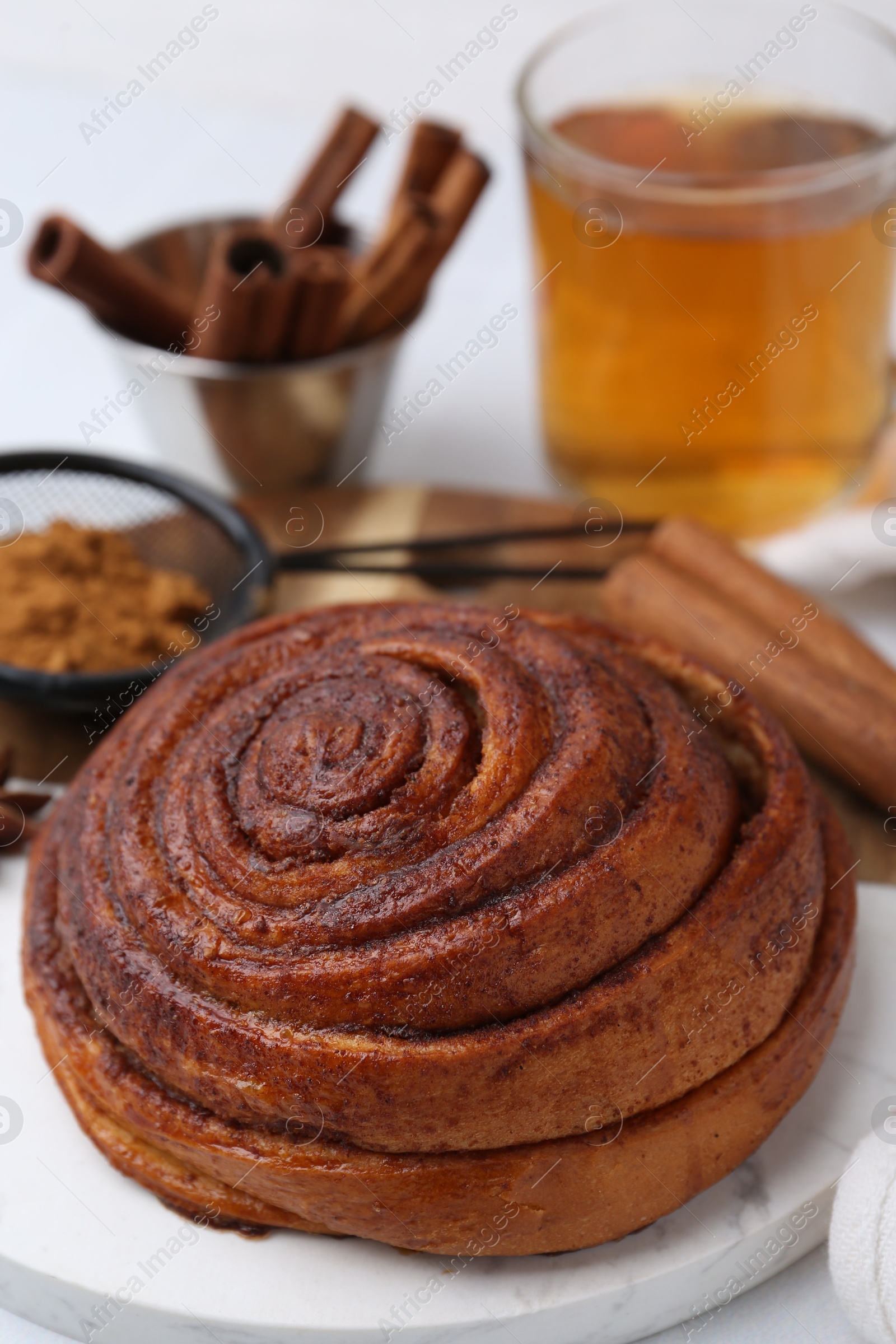 Photo of Delicious cinnamon roll bun, tea and spices on white table, closeup