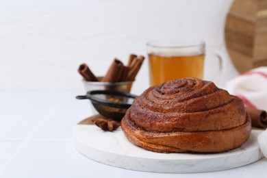 Photo of Delicious cinnamon roll bun, tea and spices on white table, closeup. Space for text