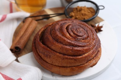 Photo of Delicious cinnamon roll bun and spices on white table, closeup