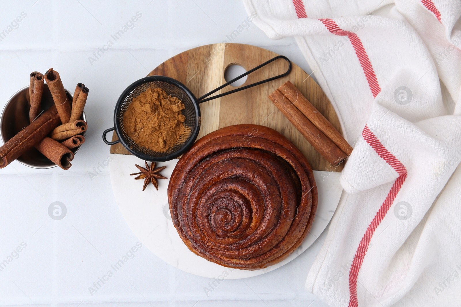 Photo of Delicious cinnamon roll bun and spices on white tiled table, flat lay