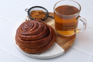 Photo of Delicious cinnamon roll bun, tea and spices on white tiled table, closeup