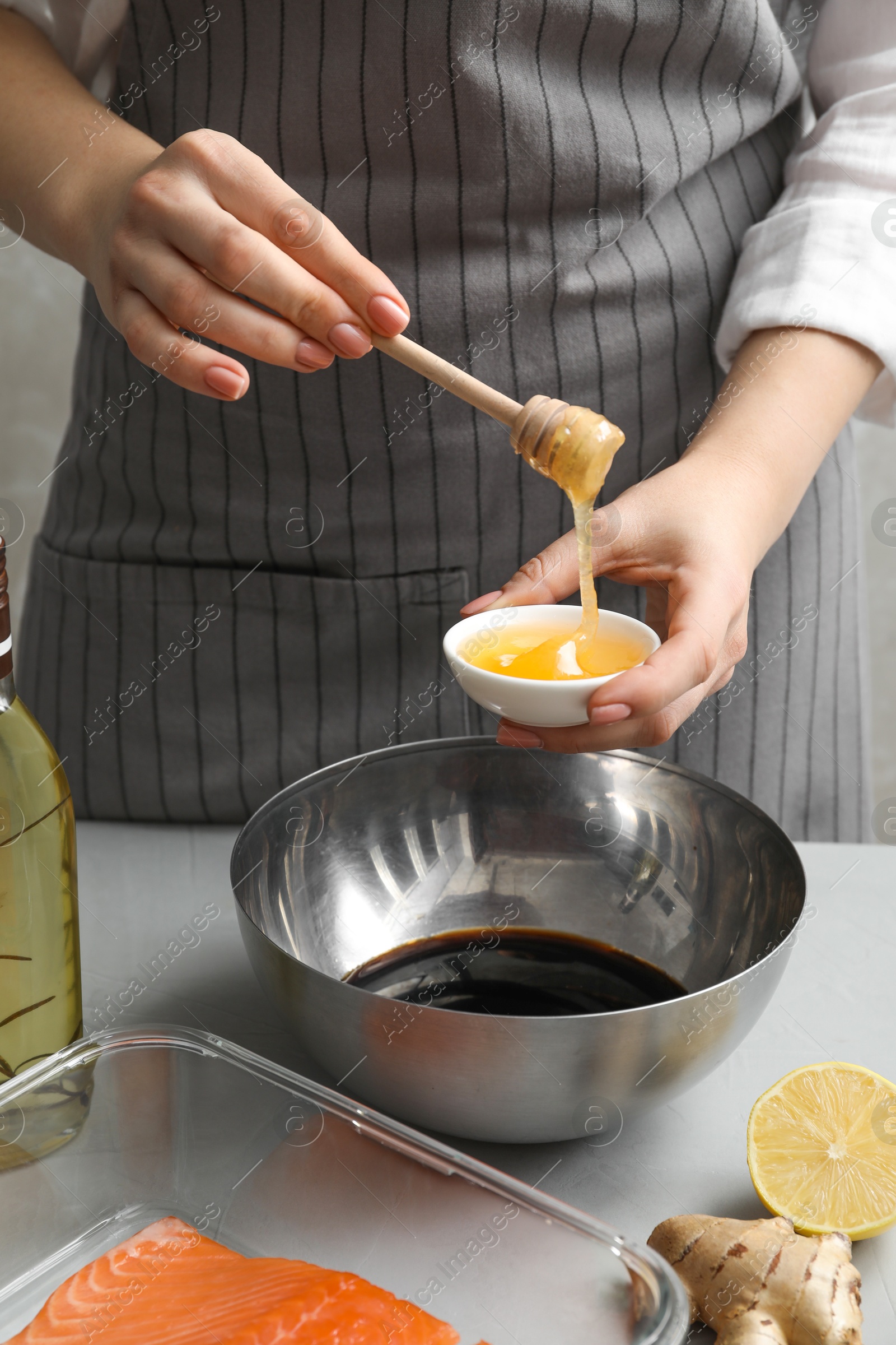 Photo of Woman adding honey into bowl with soy sauce at gray table, closeup