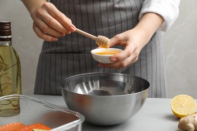 Photo of Woman adding honey at gray table, closeup