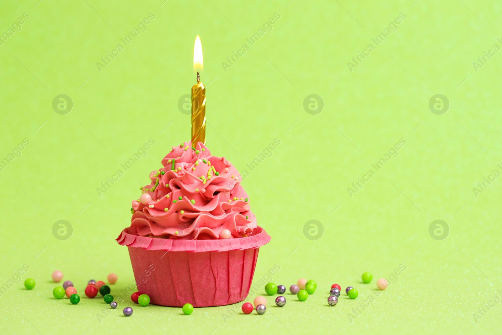 Photo of Tasty cupcake with burning candle on light green background, space for text