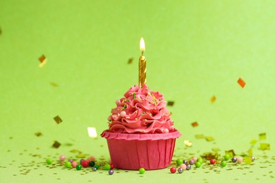 Photo of Tasty cupcake with burning candle on light green background