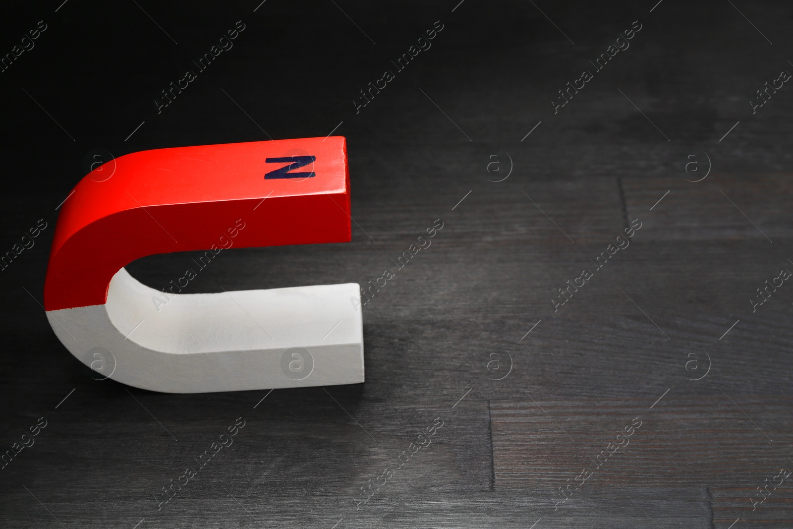 Photo of One horseshoe magnet on black wooden table, space for text