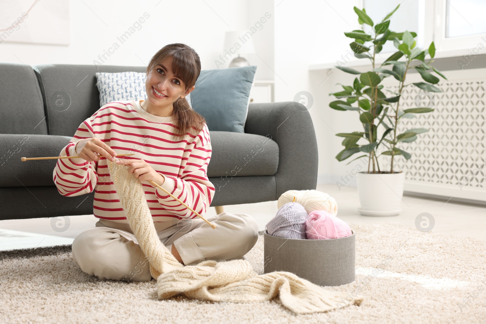 Photo of Beautiful woman knitting with needles on floor at home