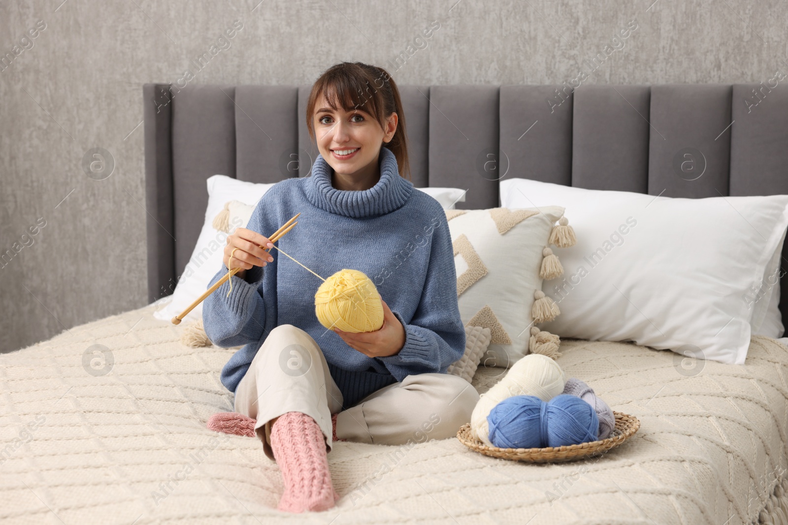 Photo of Beautiful woman knitting with needles on bed at home