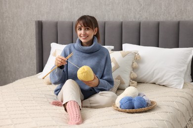 Beautiful woman knitting with needles on bed at home