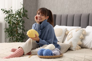 Beautiful woman with colorful yarns on bed at home. Knitting material