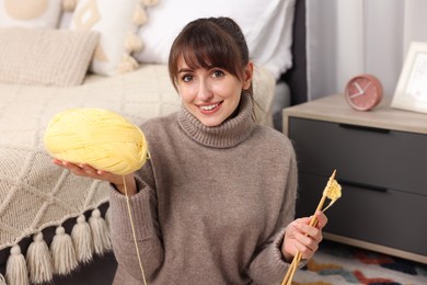 Photo of Beautiful woman with yellow yarn and knitting needles on floor at home