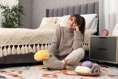 Photo of Beautiful woman with colorful yarns and knitting needles on floor at home