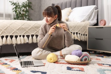 Photo of Woman learning to knit with online course on floor at home