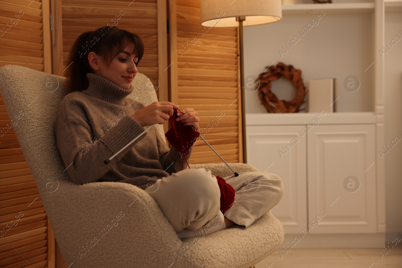 Photo of Beautiful woman knitting with needles in armchair at home