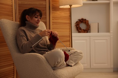 Photo of Beautiful woman knitting with needles in armchair at home