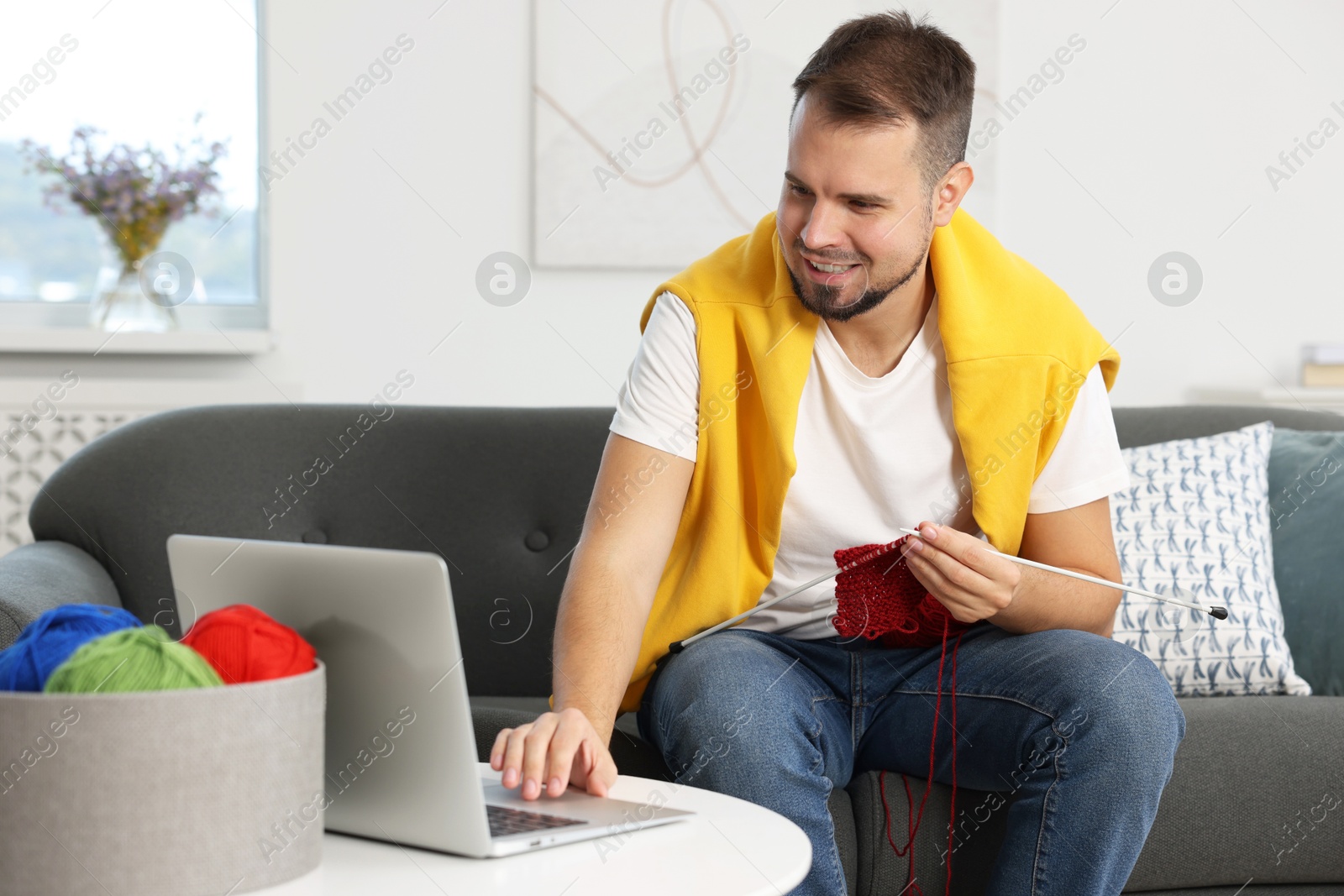 Photo of Man learning to knit with online course on sofa at home