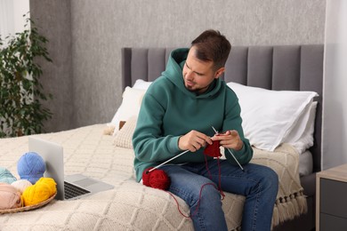 Man learning to knit with online course on bed at home