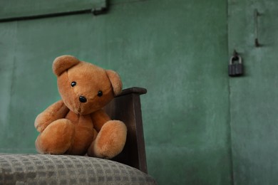 Photo of Lonely teddy bear on old bed near green wall outdoors