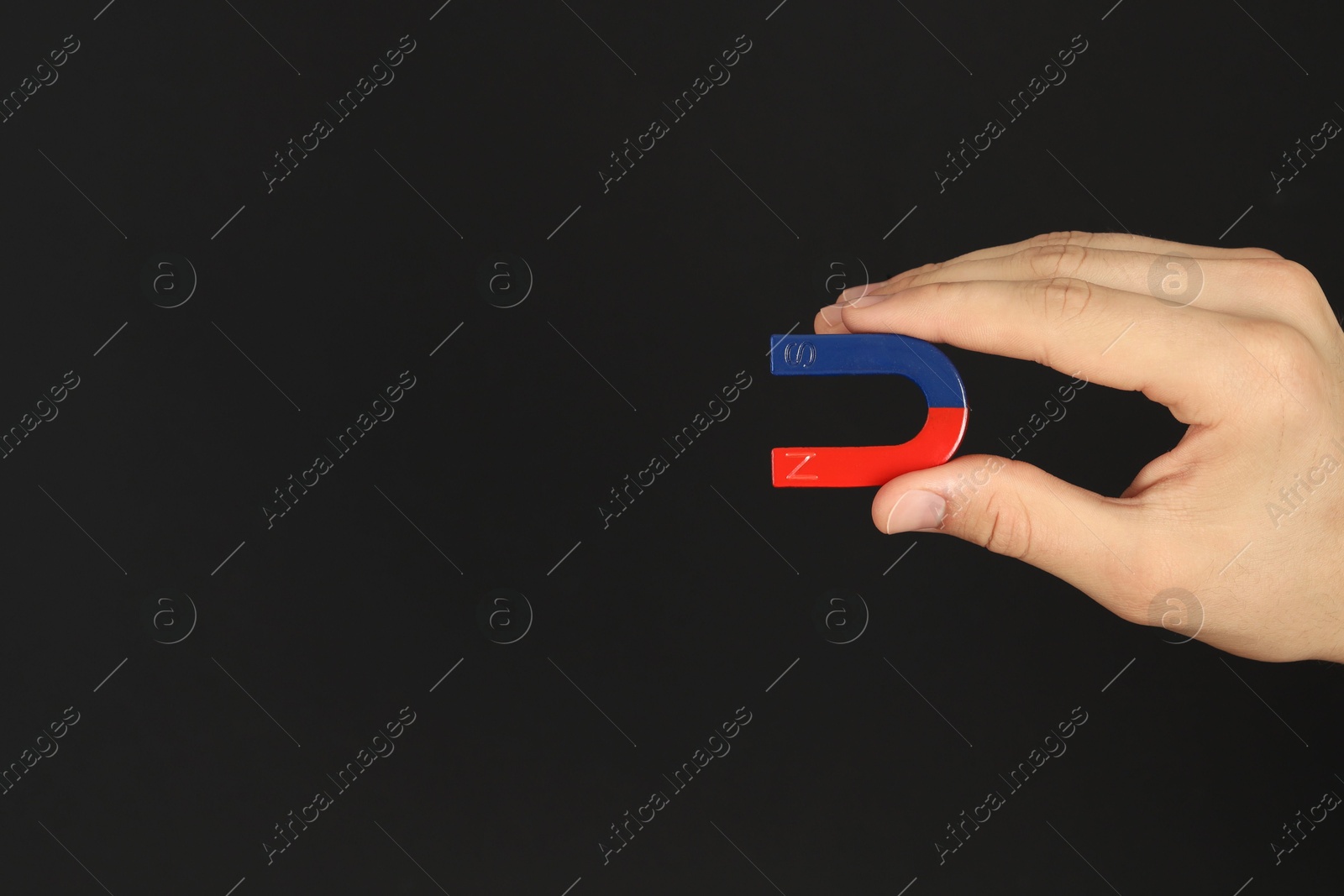 Photo of Man holding horseshoe magnet on dark background, closeup. Space for text