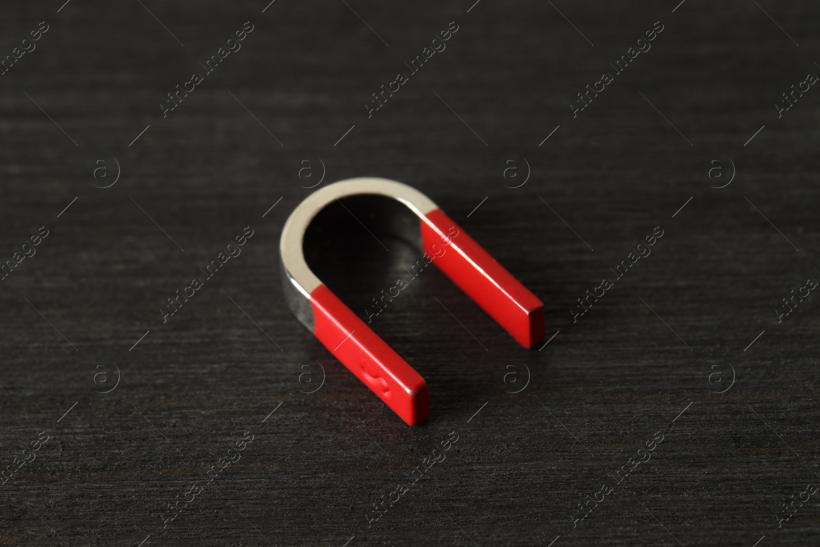 Photo of One horseshoe magnet on black wooden table, closeup