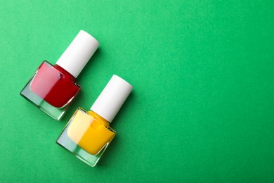 Photo of Bright nail polishes in bottles on green background, flat lay. Space for text