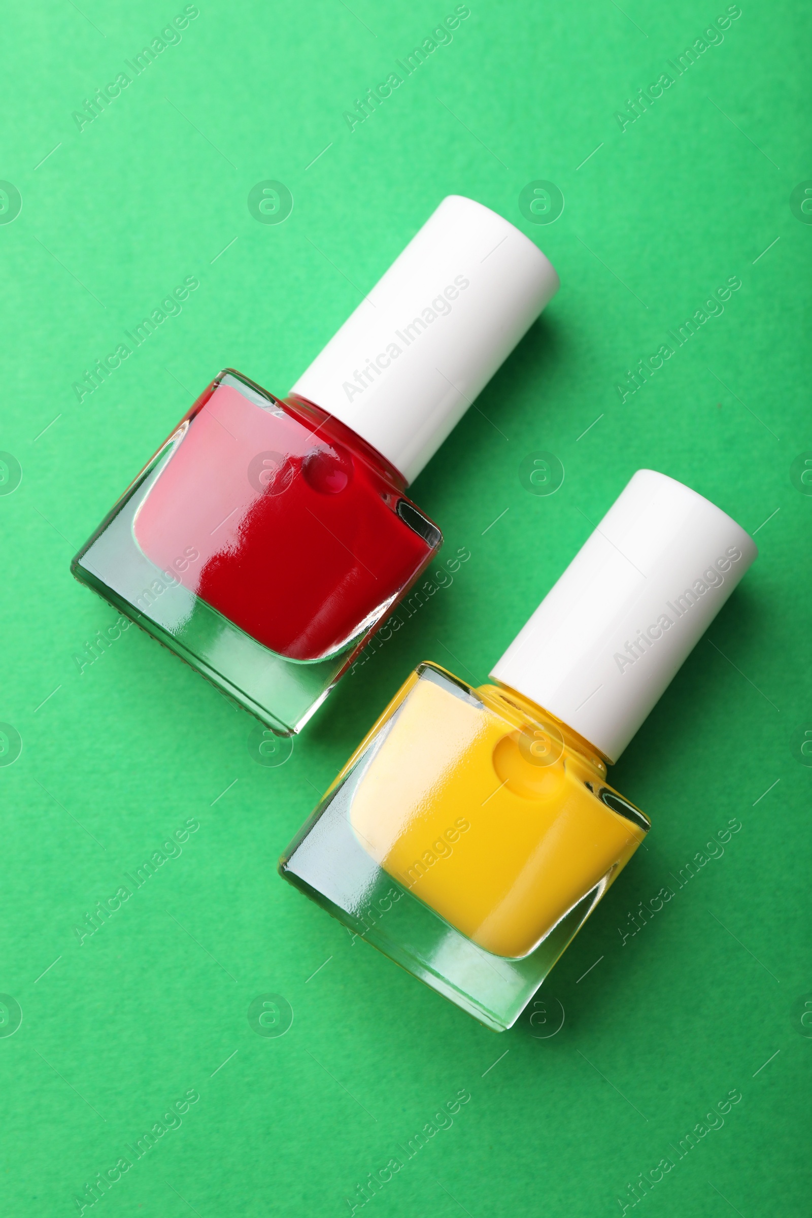 Photo of Bright nail polishes in bottles on green background, flat lay