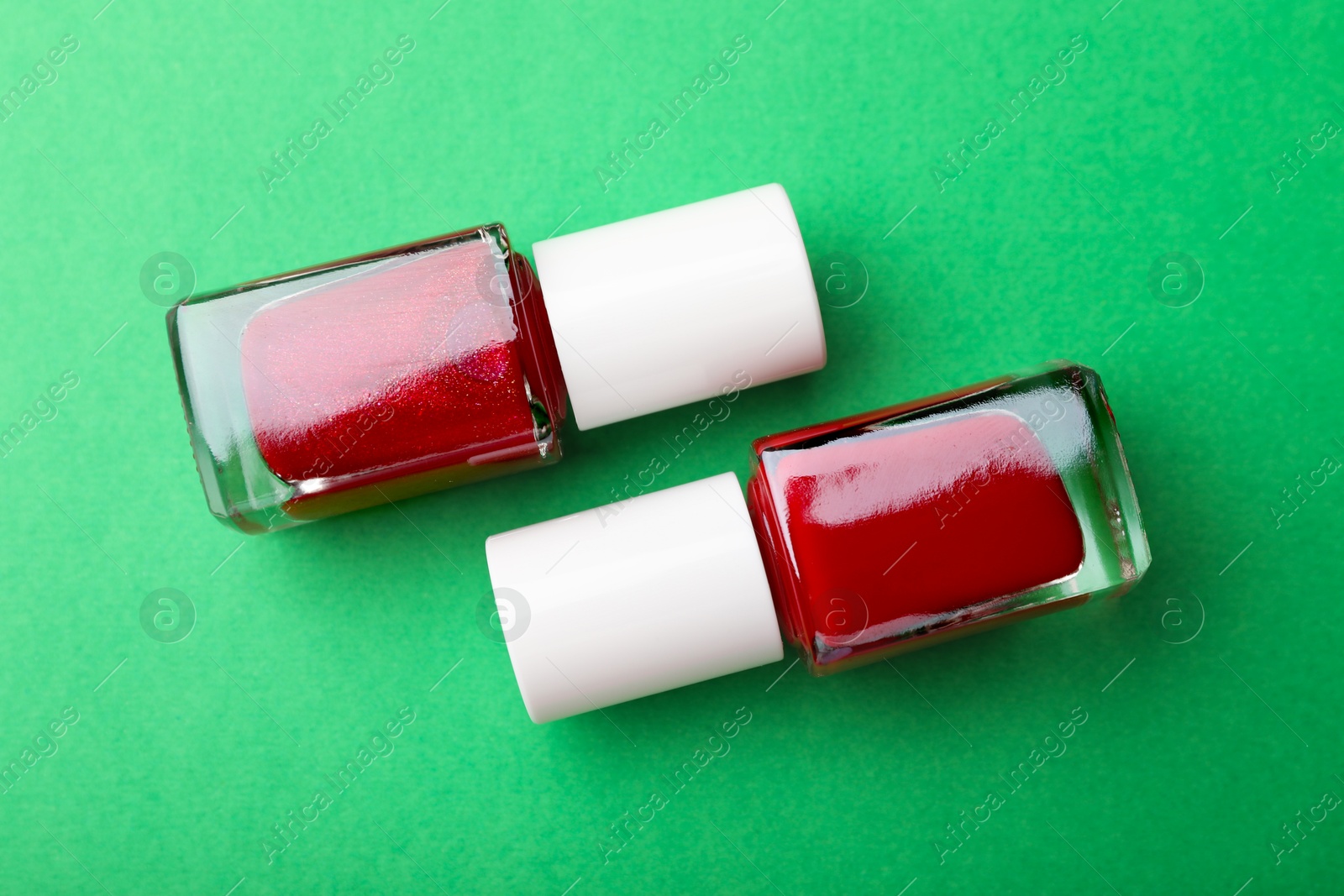 Photo of Red nail polishes in bottles on green background, flat lay