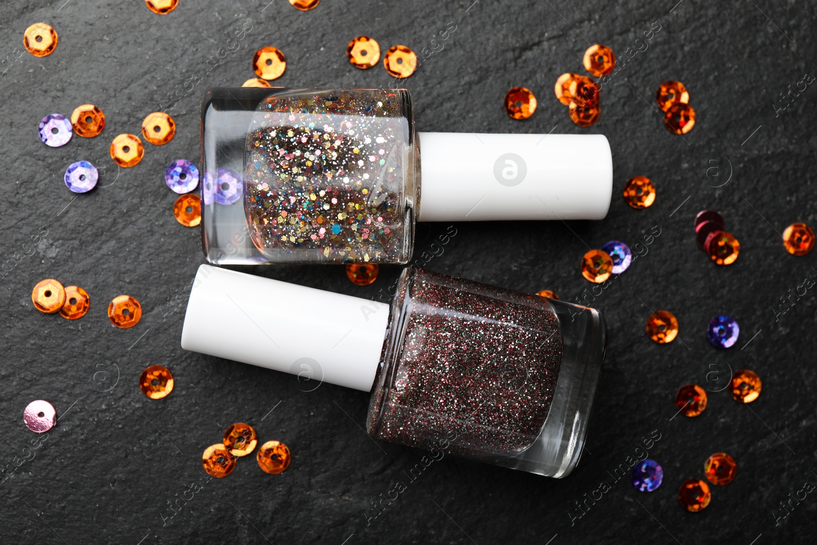 Photo of Glitter nail polishes in bottles on dark textured table, flat lay