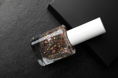 Photo of Glitter nail polish in bottle on dark textured table, above view