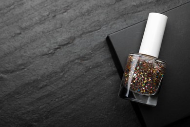 Photo of Glitter nail polish in bottle on dark textured table, top view. Space for text