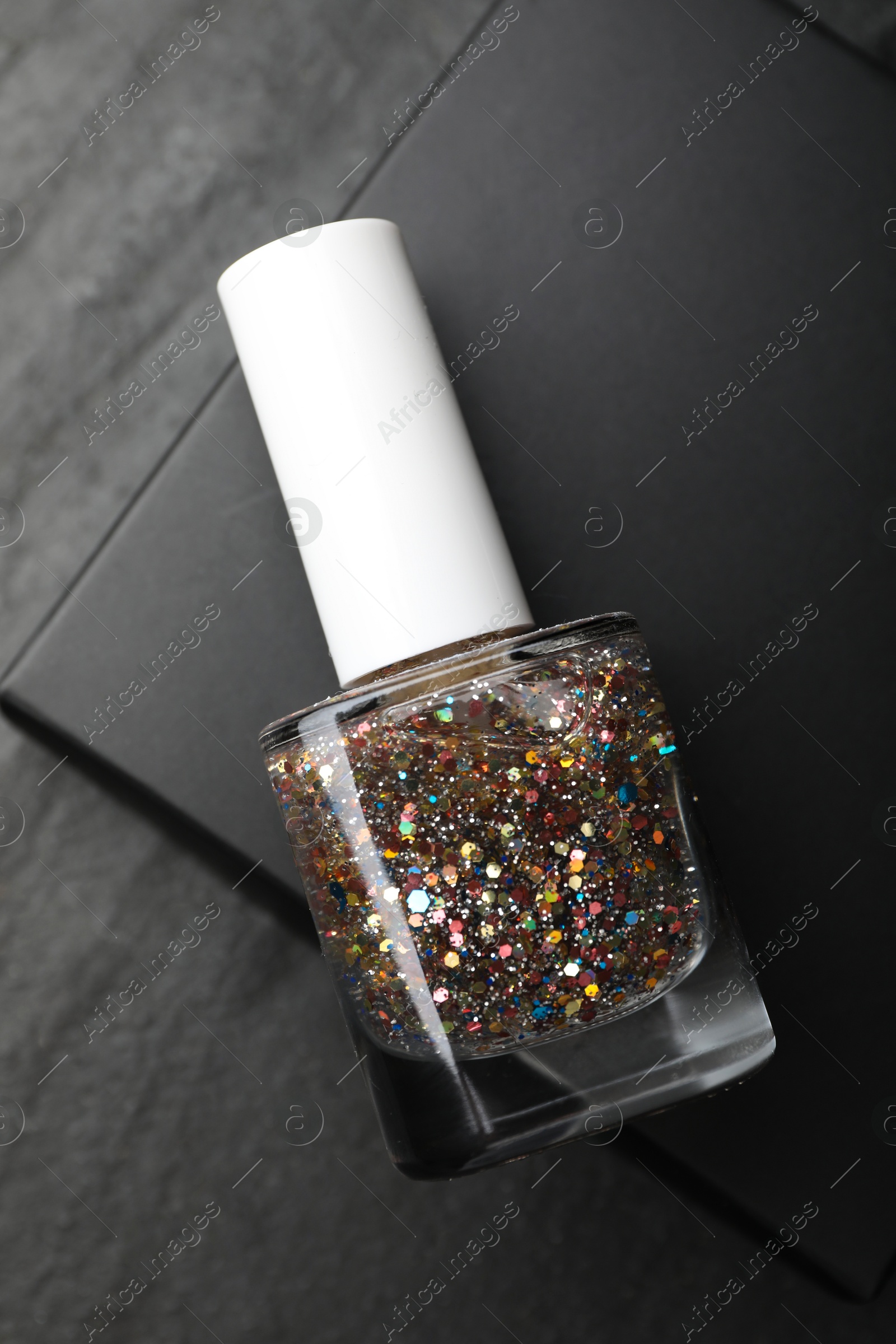 Photo of Glitter nail polish in bottle on dark textured table, top view