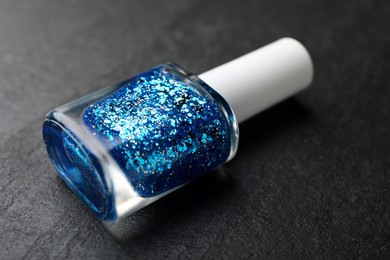 Photo of Glitter nail polish in bottle on dark textured table, closeup