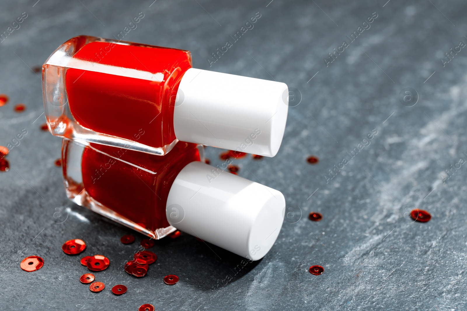 Photo of Red nail polishes in bottles on grey textured table, closeup