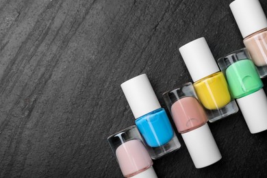 Photo of Set of different nail polishes in bottles on dark textured table, flat lay. Space for text