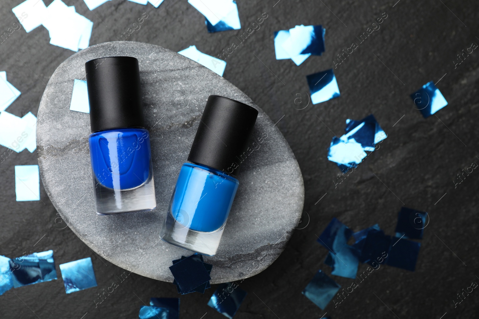 Photo of Stylish presentation of blue nail polishes in bottles on dark textured table, flat lay. Space for text