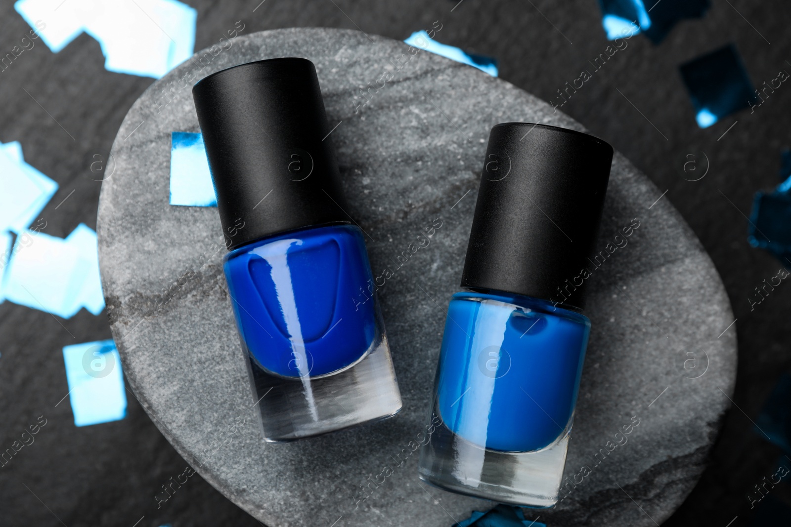 Photo of Stylish presentation of blue nail polishes in bottles on dark textured table, flat lay