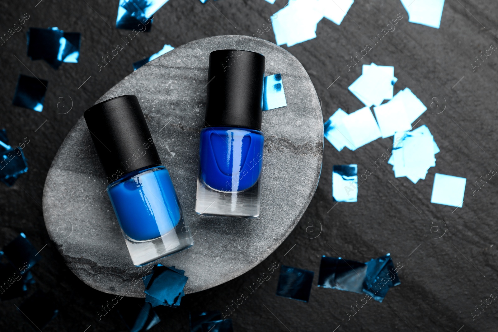 Photo of Stylish presentation of blue nail polishes in bottles on dark textured table, flat lay. Space for text