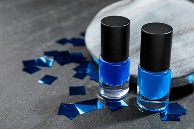 Photo of Stylish presentation of blue nail polishes in bottles on grey textured table, closeup. Space for text