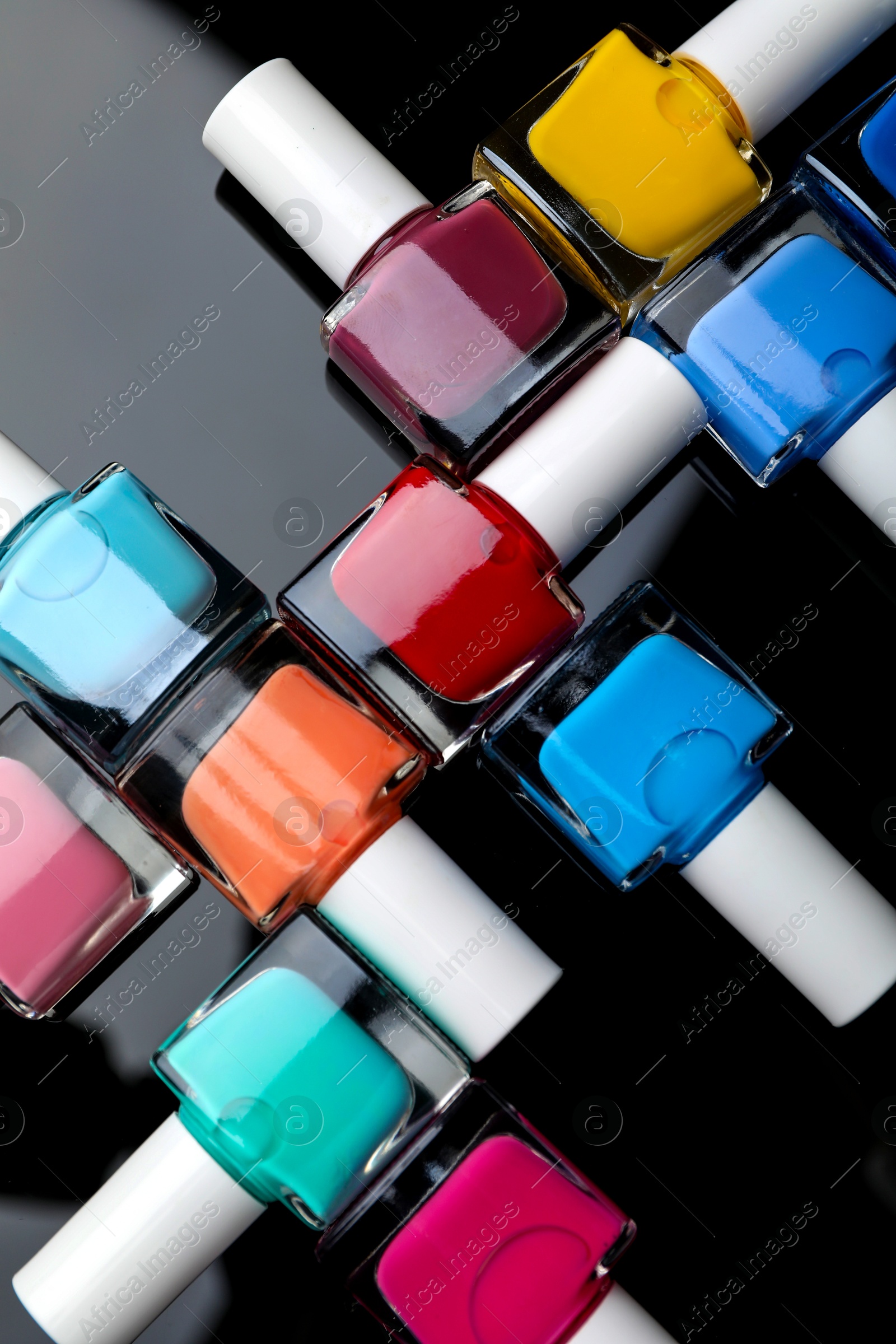 Photo of Set of different nail polishes in bottles on black mirror surface, flat lay