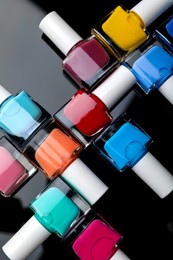 Photo of Set of different nail polishes in bottles on black mirror surface, flat lay