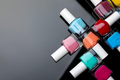 Photo of Set of different nail polishes in bottles on mirror surface, flat lay. Space for text