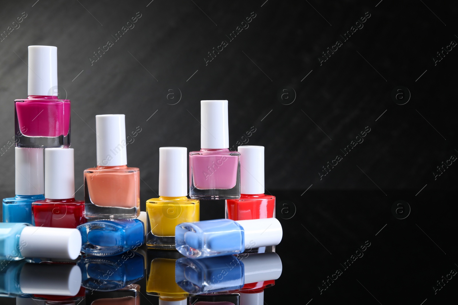 Photo of Set of different nail polishes in bottles on black mirror surface. Space for text