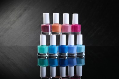 Photo of Set of different nail polishes in bottles on black mirror surface